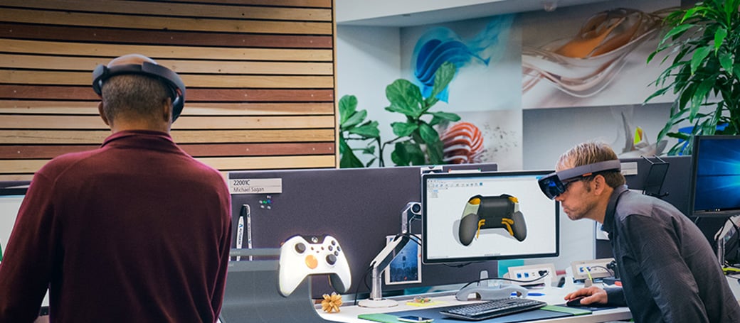 Two men wearing HoloLenses, working on a holographic Xbox controller